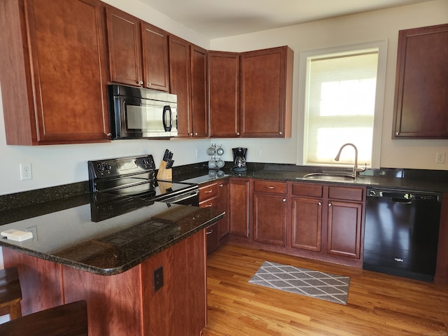 kitchen with black appliances, a kitchen bar, sink, light wood-type flooring, and dark stone counters