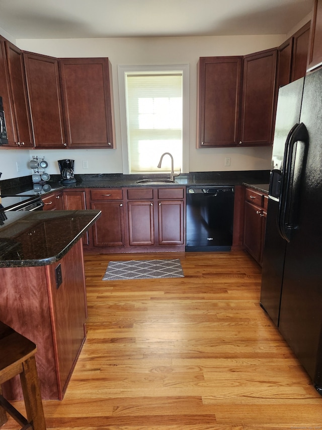 kitchen with black appliances, dark stone countertops, light hardwood / wood-style floors, and sink