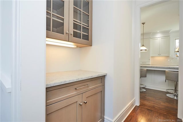 interior space featuring tasteful backsplash, light brown cabinets, hanging light fixtures, light stone countertops, and dark hardwood / wood-style floors