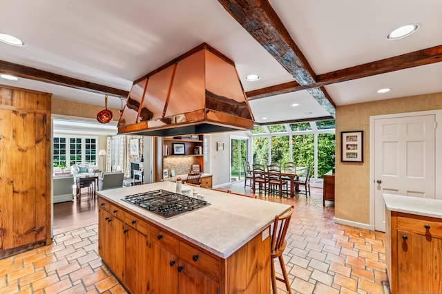 kitchen with a kitchen island, custom range hood, stainless steel gas cooktop, and beamed ceiling