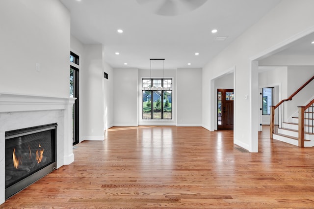 unfurnished living room with a notable chandelier, a high end fireplace, and light wood-type flooring