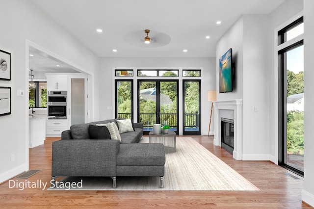 living room featuring a high end fireplace, light wood-type flooring, and a healthy amount of sunlight