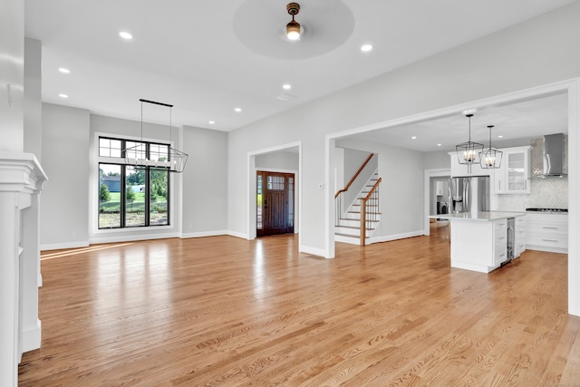 unfurnished living room with wine cooler, light wood-type flooring, and an inviting chandelier