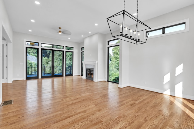 unfurnished living room with ceiling fan with notable chandelier, light hardwood / wood-style flooring, a premium fireplace, and a healthy amount of sunlight