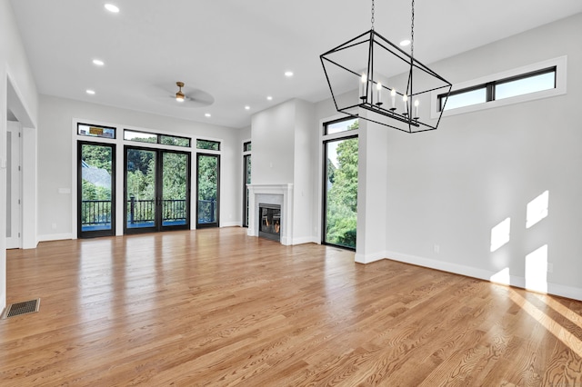 unfurnished living room with ceiling fan with notable chandelier and light hardwood / wood-style floors