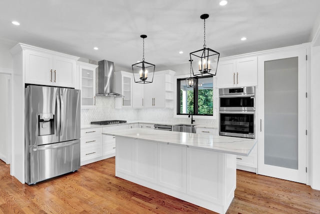 kitchen featuring appliances with stainless steel finishes, wall chimney range hood, backsplash, light wood-type flooring, and a kitchen island