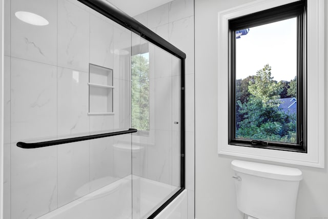 bathroom featuring enclosed tub / shower combo, toilet, and plenty of natural light