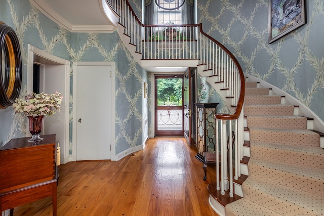 foyer with ornamental molding, wood-type flooring, and a towering ceiling