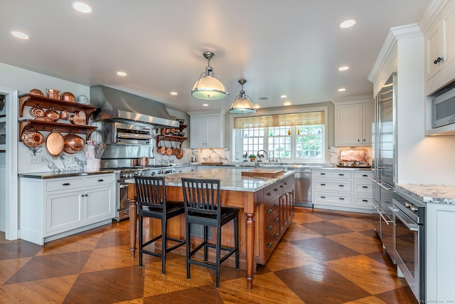 kitchen featuring white cabinets, appliances with stainless steel finishes, light stone counters, island exhaust hood, and a kitchen island