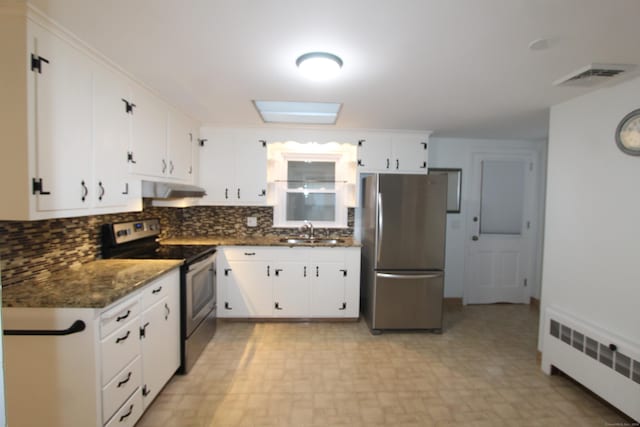 kitchen with appliances with stainless steel finishes, a skylight, radiator, sink, and dark stone countertops