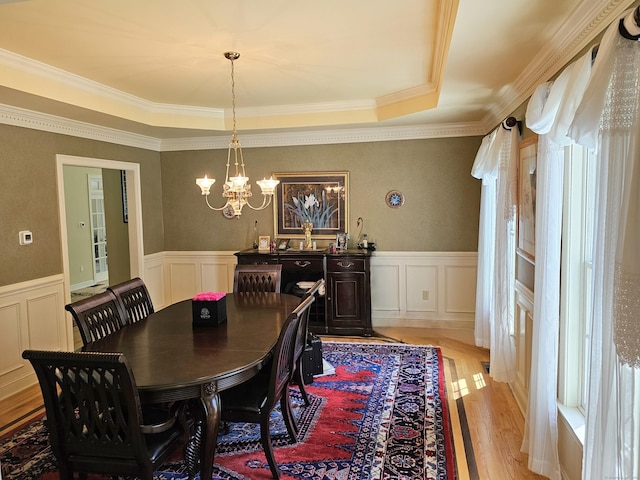 dining area with a notable chandelier, crown molding, a raised ceiling, and light wood-type flooring