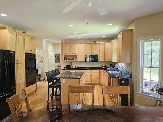 kitchen featuring light brown cabinetry, sink, a kitchen island, light hardwood / wood-style floors, and black appliances