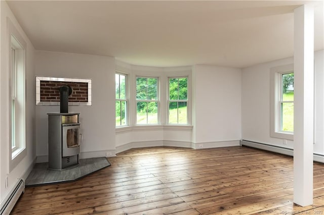 unfurnished living room featuring a wood stove, baseboard heating, and hardwood / wood-style flooring