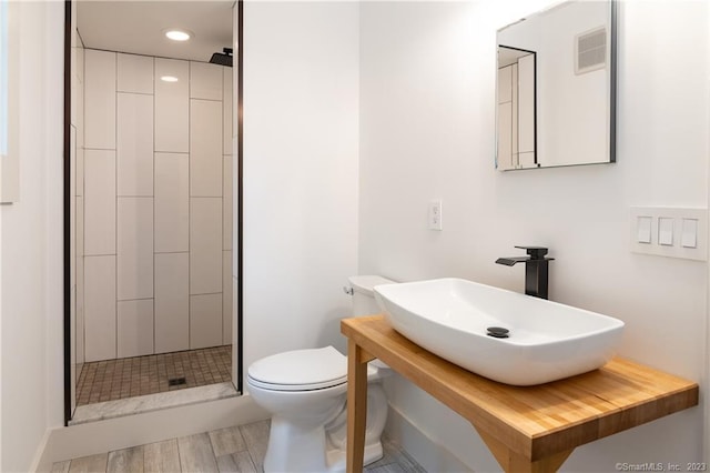 bathroom featuring sink, hardwood / wood-style flooring, tiled shower, and toilet