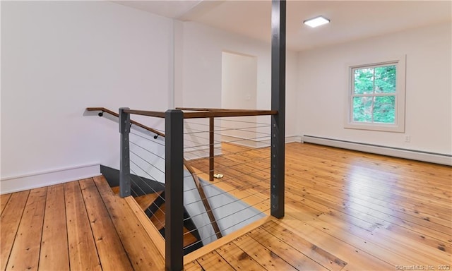 stairway featuring a baseboard heating unit and wood-type flooring