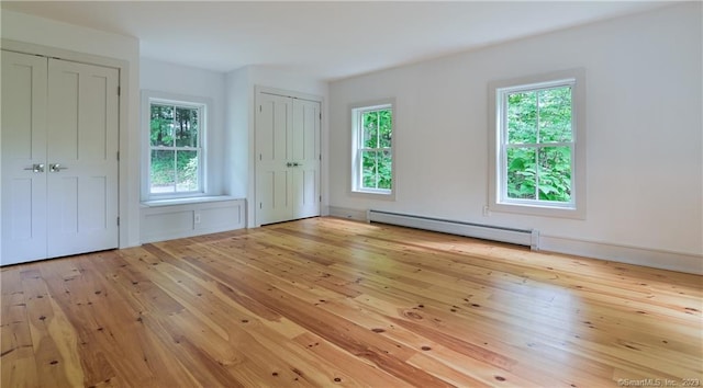 interior space with a baseboard heating unit, light wood-type flooring, and multiple closets