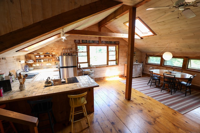 kitchen featuring tile counters, a wealth of natural light, stainless steel refrigerator, and lofted ceiling with skylight