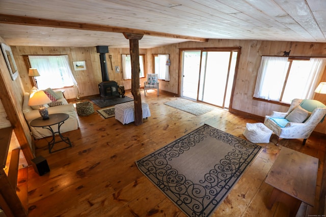 living room featuring beamed ceiling, hardwood / wood-style floors, wood walls, and a wood stove