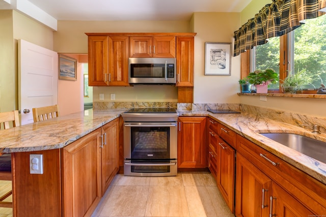 kitchen with appliances with stainless steel finishes, kitchen peninsula, light stone countertops, and a kitchen breakfast bar