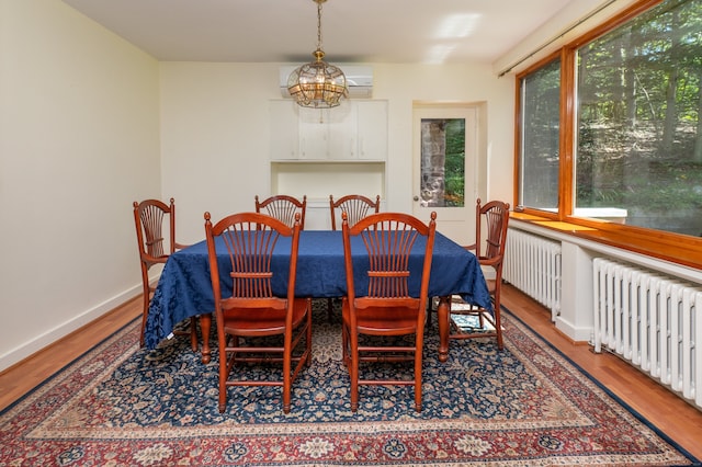 dining area featuring an inviting chandelier, radiator heating unit, wood-type flooring, and a wall unit AC