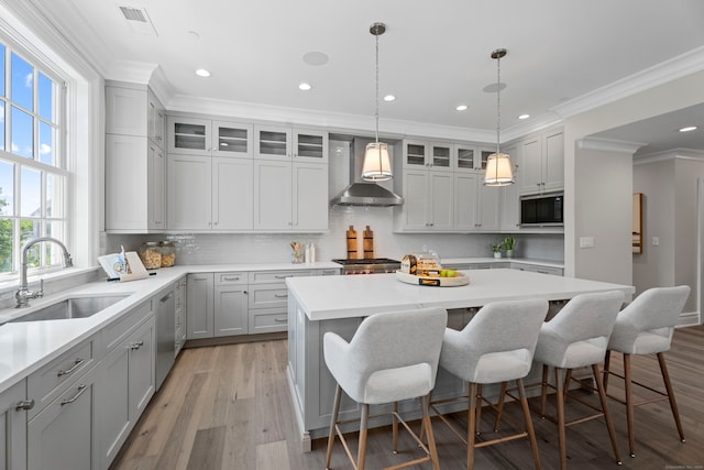 kitchen featuring stainless steel appliances, sink, light hardwood / wood-style flooring, a center island, and wall chimney exhaust hood