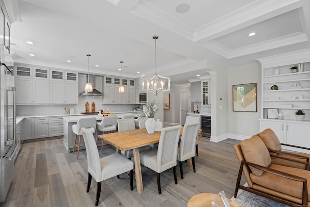 dining room with a notable chandelier, wine cooler, ornamental molding, light hardwood / wood-style floors, and a raised ceiling