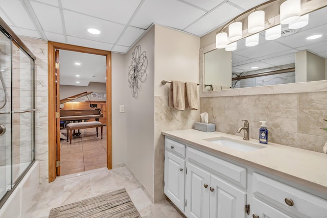 bathroom with bath / shower combo with glass door, a drop ceiling, recessed lighting, marble finish floor, and vanity