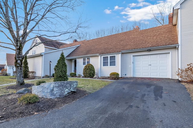 single story home featuring aphalt driveway, an attached garage, roof with shingles, and a chimney