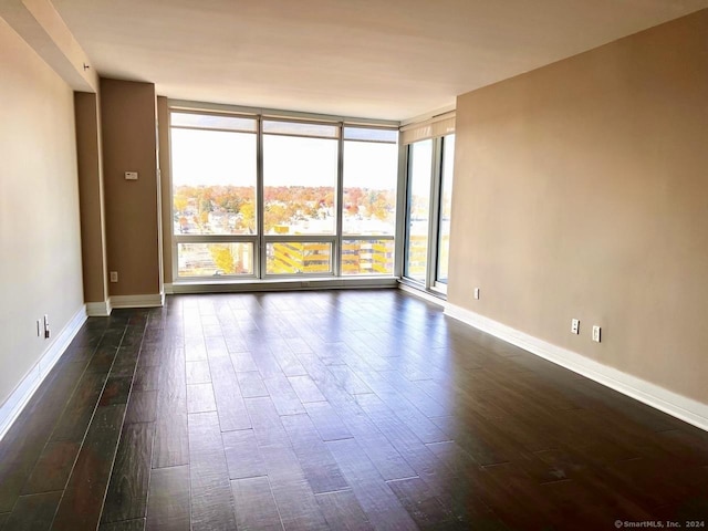 empty room with expansive windows, dark wood finished floors, and baseboards