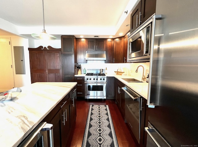 kitchen featuring stainless steel appliances, light countertops, under cabinet range hood, pendant lighting, and a sink