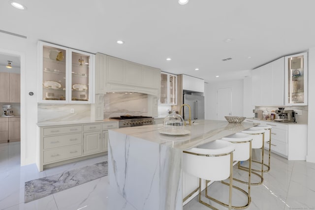 kitchen with white cabinets, light stone countertops, stainless steel appliances, a center island with sink, and tasteful backsplash