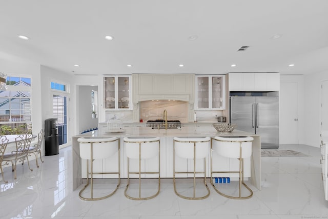 kitchen featuring white cabinetry, tasteful backsplash, a kitchen breakfast bar, built in fridge, and a center island with sink