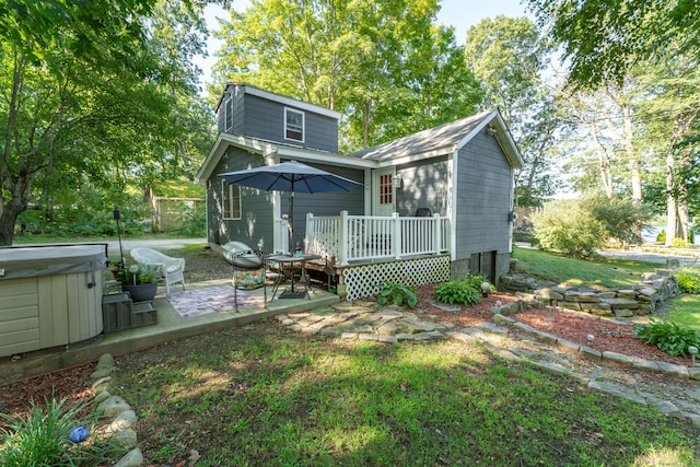 back of property with a hot tub, a patio, a yard, and a deck