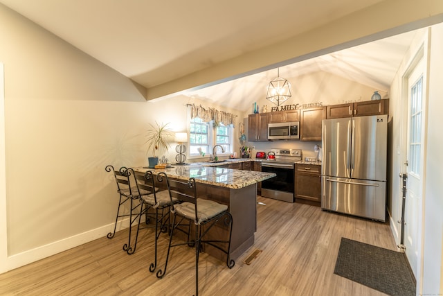 kitchen with stainless steel appliances, vaulted ceiling, a breakfast bar, pendant lighting, and light hardwood / wood-style flooring