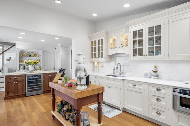 bar featuring light stone countertops, white cabinets, beverage cooler, sink, and oven