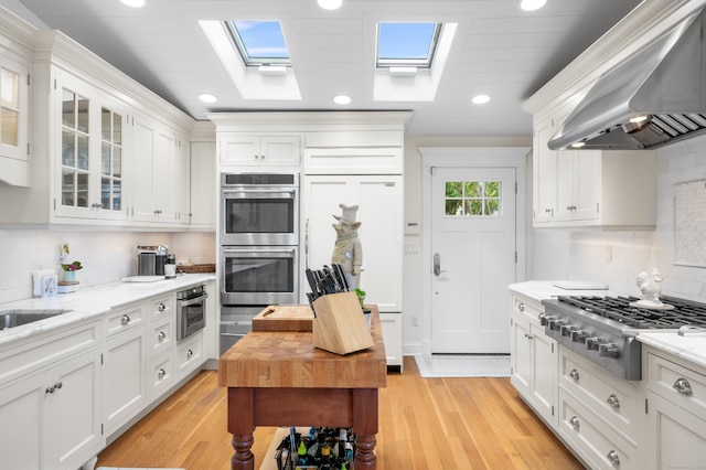 kitchen with appliances with stainless steel finishes, extractor fan, light stone counters, and white cabinetry