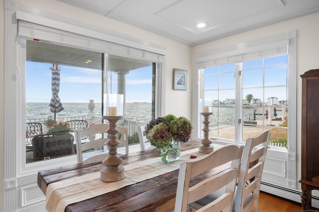 dining space featuring a baseboard radiator, hardwood / wood-style floors, ornamental molding, and a water view