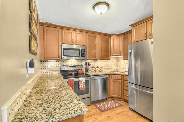 kitchen featuring appliances with stainless steel finishes, light hardwood / wood-style flooring, tasteful backsplash, sink, and light stone counters