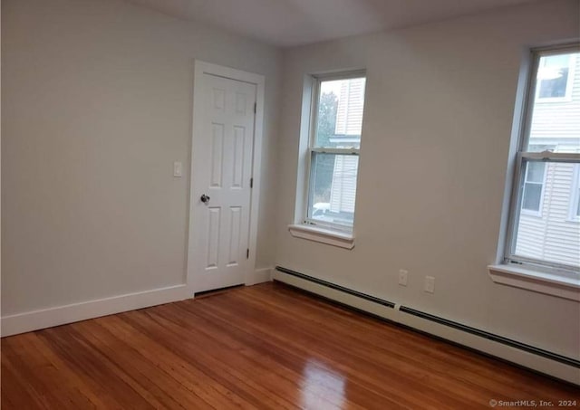 empty room featuring a wealth of natural light, a baseboard heating unit, and hardwood / wood-style flooring