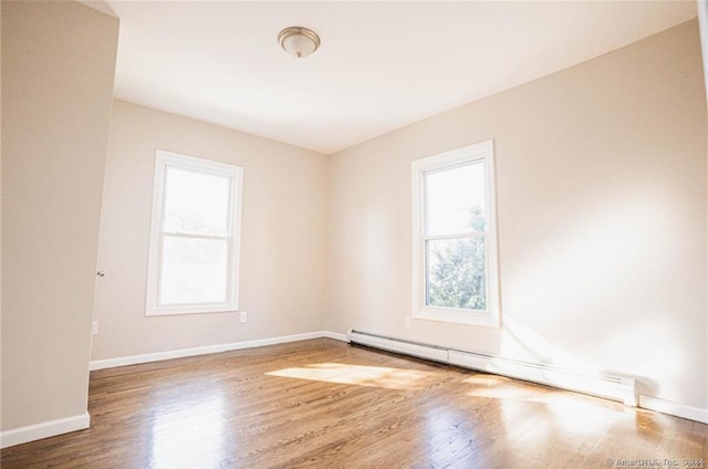 spare room with baseboard heating, hardwood / wood-style flooring, and plenty of natural light