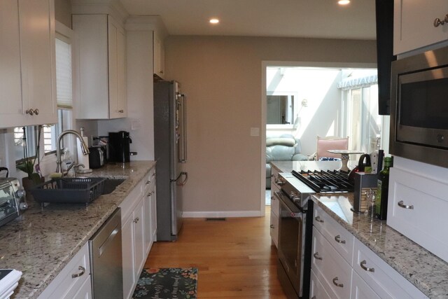 kitchen featuring sink, light hardwood / wood-style flooring, a healthy amount of sunlight, white cabinetry, and stainless steel appliances