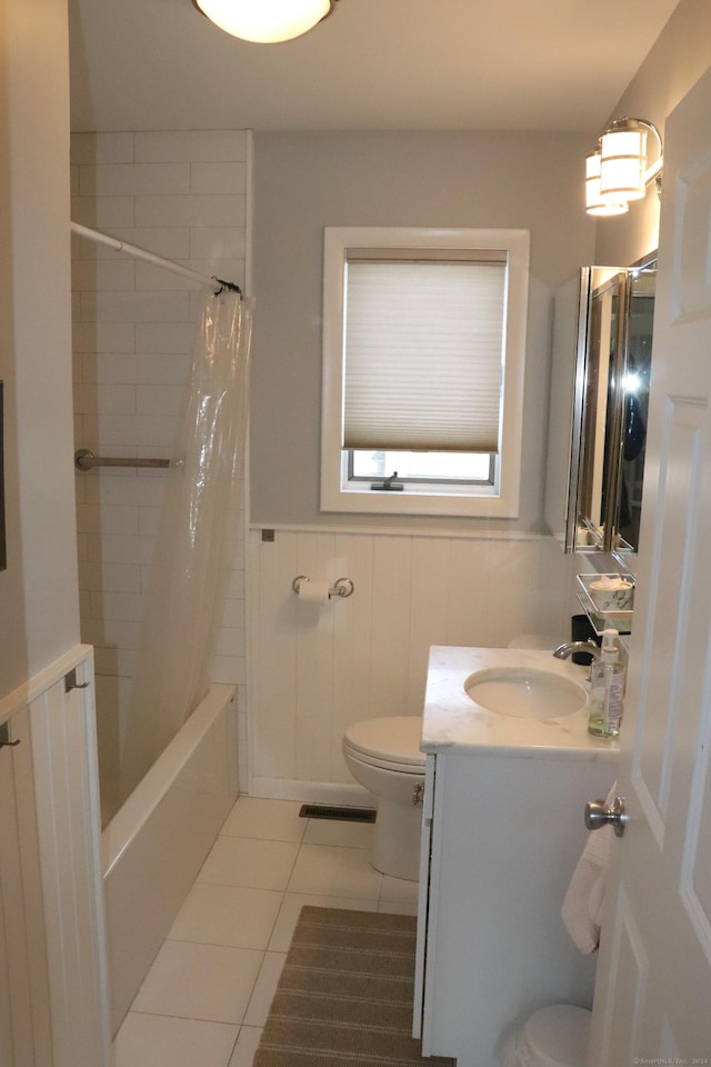 full bath with toilet, vanity, wainscoting, tile patterned floors, and shower / bath combo