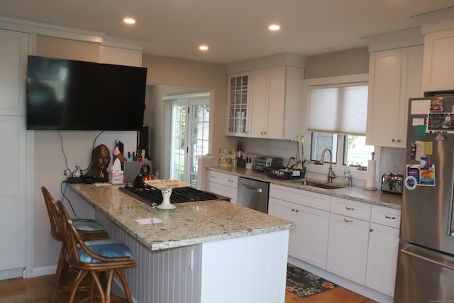 kitchen featuring glass insert cabinets, appliances with stainless steel finishes, a peninsula, white cabinetry, and a sink