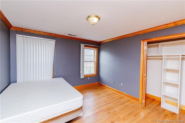 unfurnished bedroom with a closet, crown molding, and light hardwood / wood-style floors