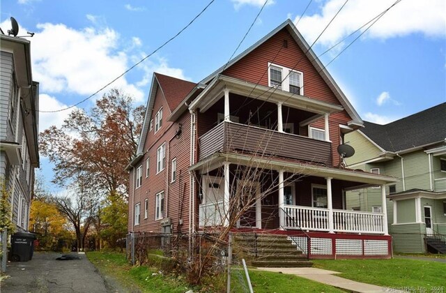 front facade with a front lawn, a balcony, and a porch