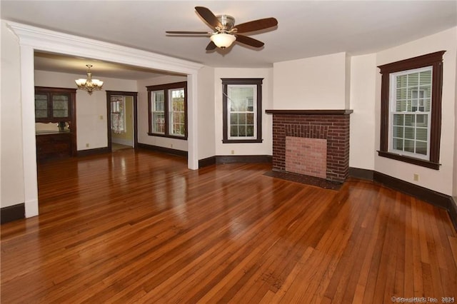 unfurnished living room with dark wood-type flooring, a brick fireplace, and ceiling fan with notable chandelier