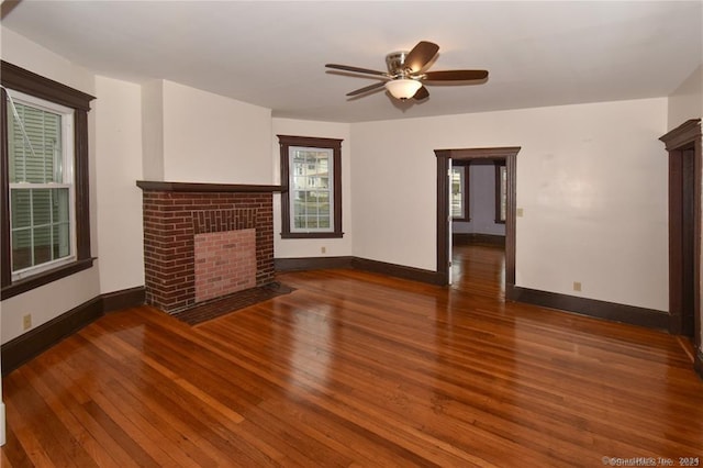 unfurnished living room featuring ceiling fan, a brick fireplace, and wood-type flooring