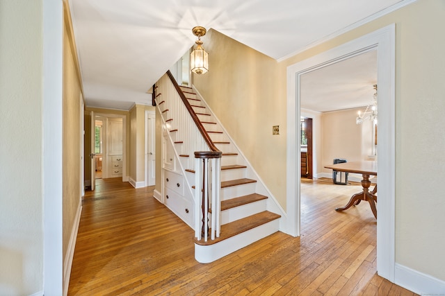 staircase featuring crown molding, wood-type flooring, a notable chandelier, and plenty of natural light