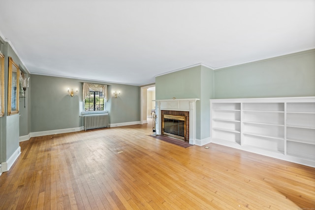 unfurnished living room with a brick fireplace, light hardwood / wood-style floors, and radiator