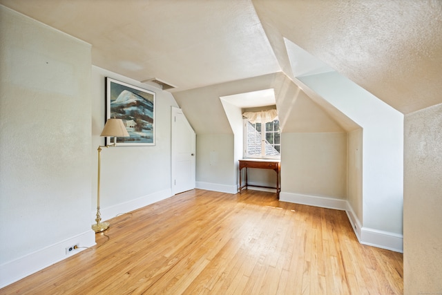 additional living space with light wood-type flooring, vaulted ceiling, and a textured ceiling